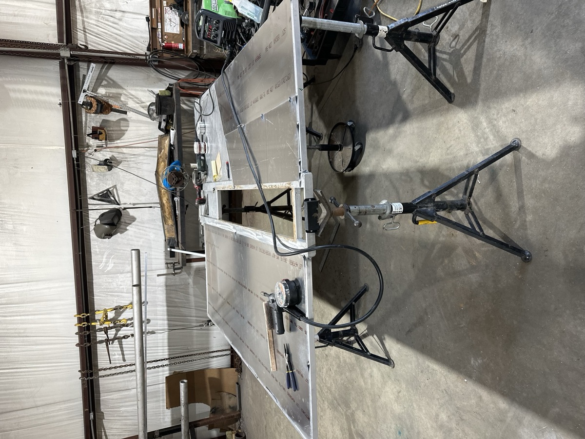 Large aluminum panel being fabricated on jack stands with TIG welder nearby