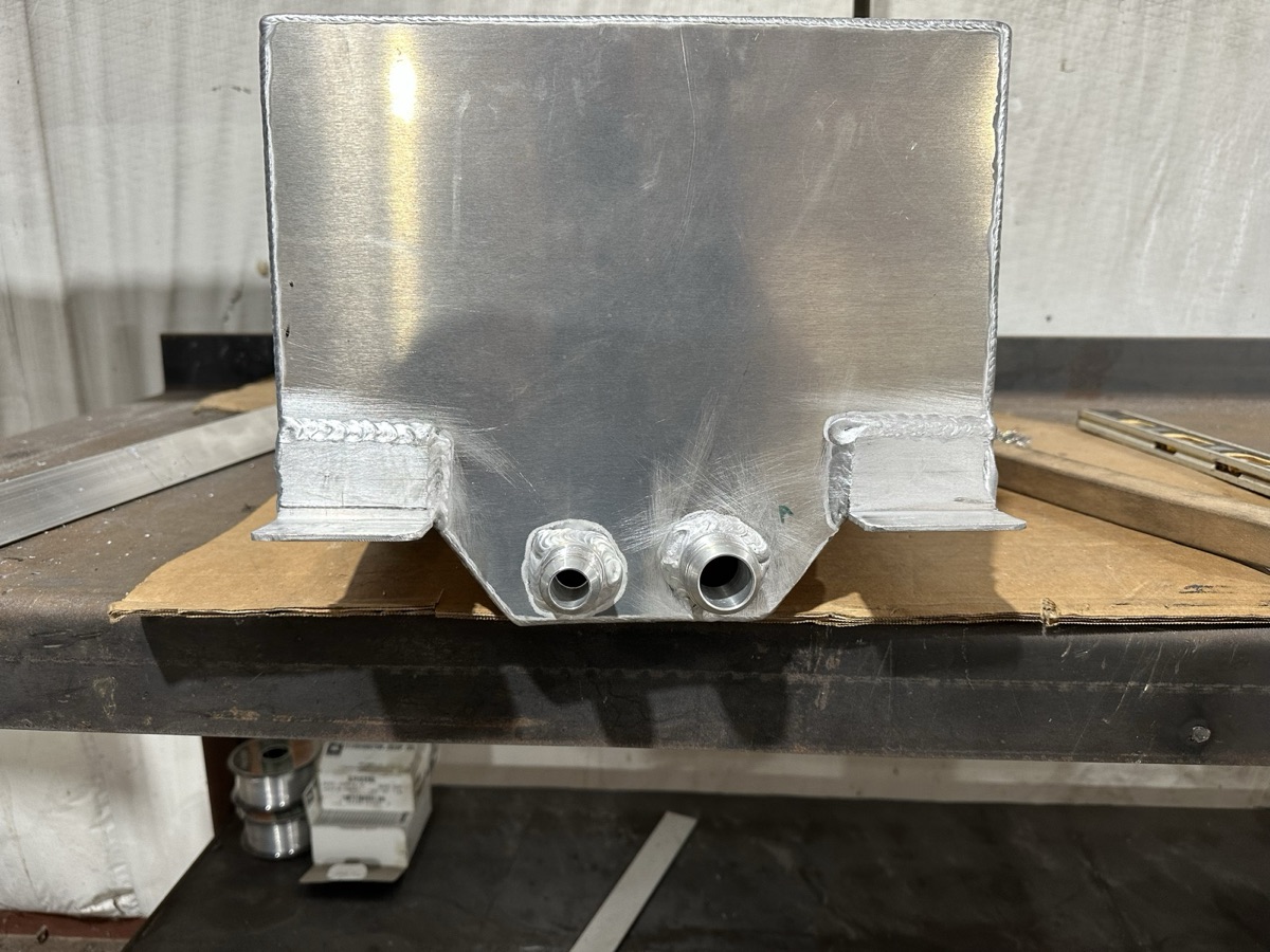 Custom-fabricated aluminum bracket with welded fittings on a workbench