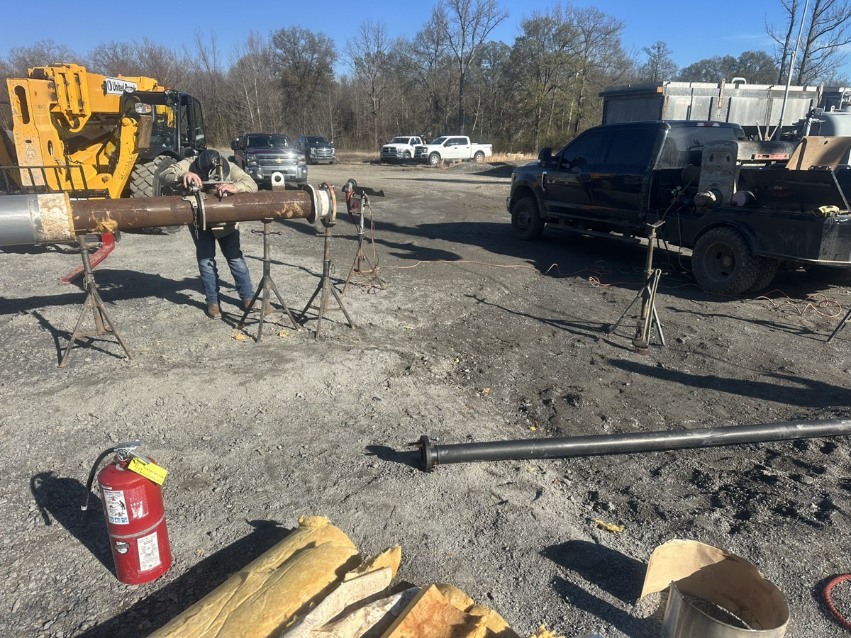 Welder doing field pipe welding next to a loader at an outdoor job site