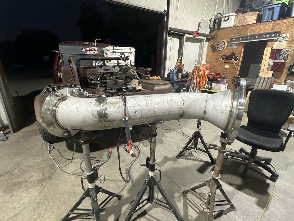 Large stainless steel pipe assembly on jack stands at night in the shop