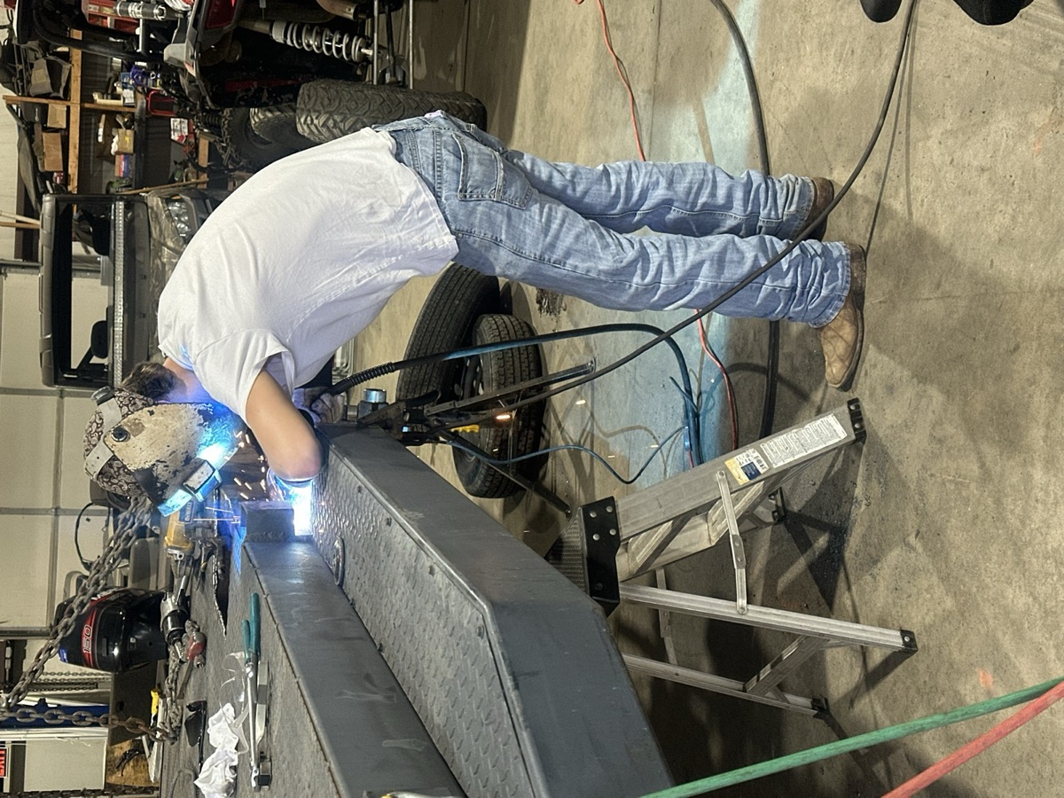 Welder in helmet welding on an aluminum boat hull in the shop