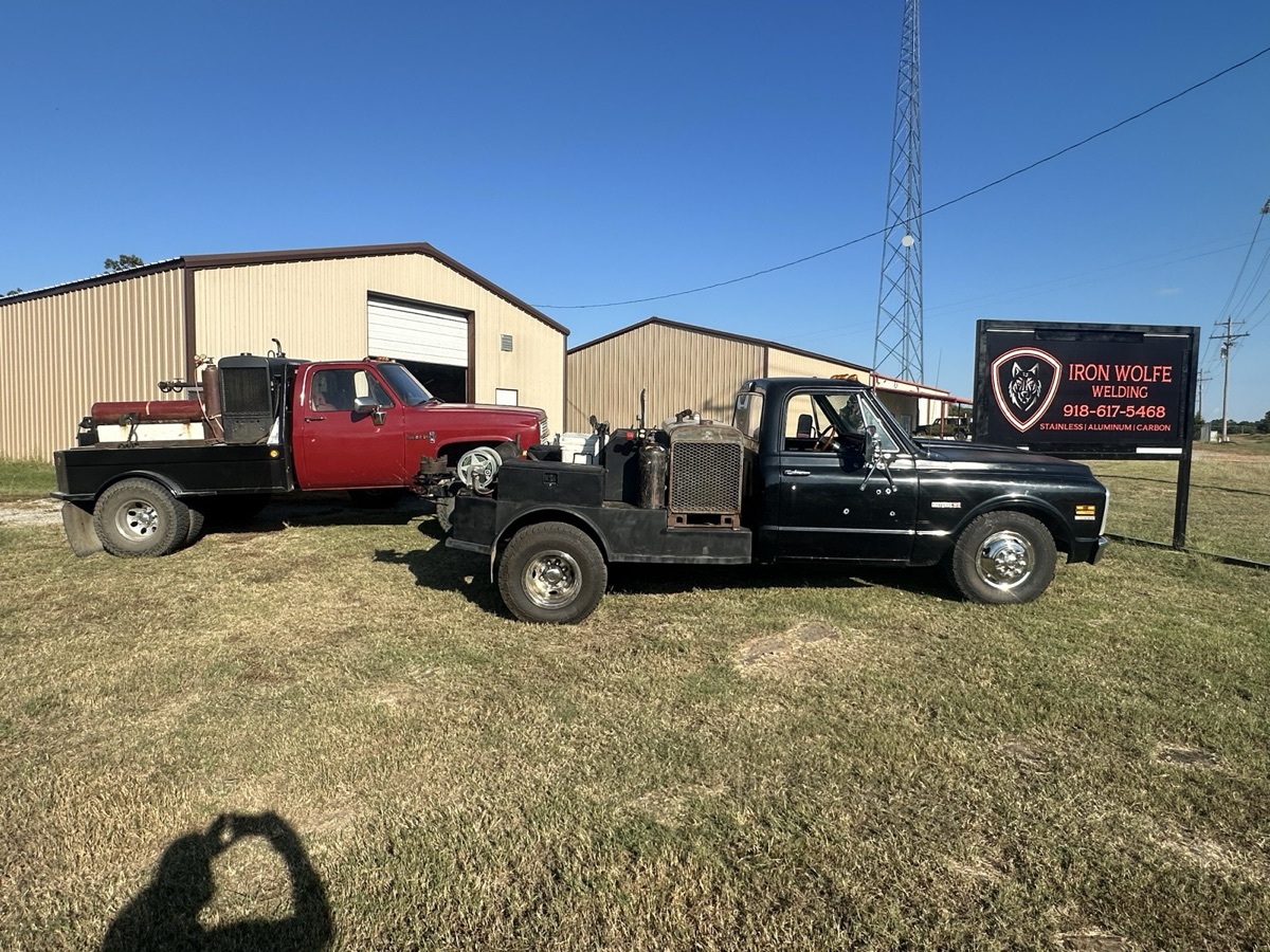 Two Iron Wolfe welding trucks parked in front of the shop sign